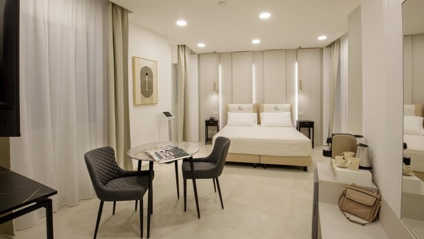 Habitación de hotel con una cama, dos sillas, una mesa, televisor, mesita de noche con lámpara y espejo.