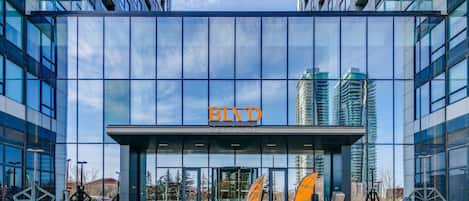 Un bâtiment moderne à la façade vitrée, sur lequel le nom « BLYD » est clairement affiché au-dessus de l’entrée, et un escalier menant à l’entrée.