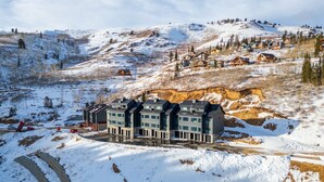Un hotel moderno con fachada simétrica, ubicado en una ladera nevada y vistas a montañas circundantes y otros edificios.