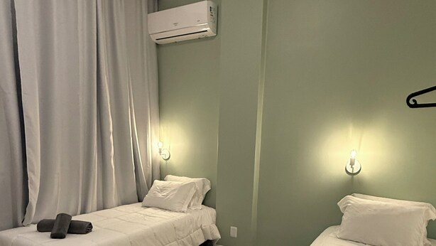 Ein Hotelzimmer mit zwei Einzelbetten, einem Nachttisch aus Holz, einer wandmontierten Klimaanlage und einer Wandleuchte.