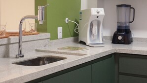Eine Küche mit integriertem Spülbecken, einer weißen Kaffeemaschine, einem schwarzen Mixer und einer grünen Wand.