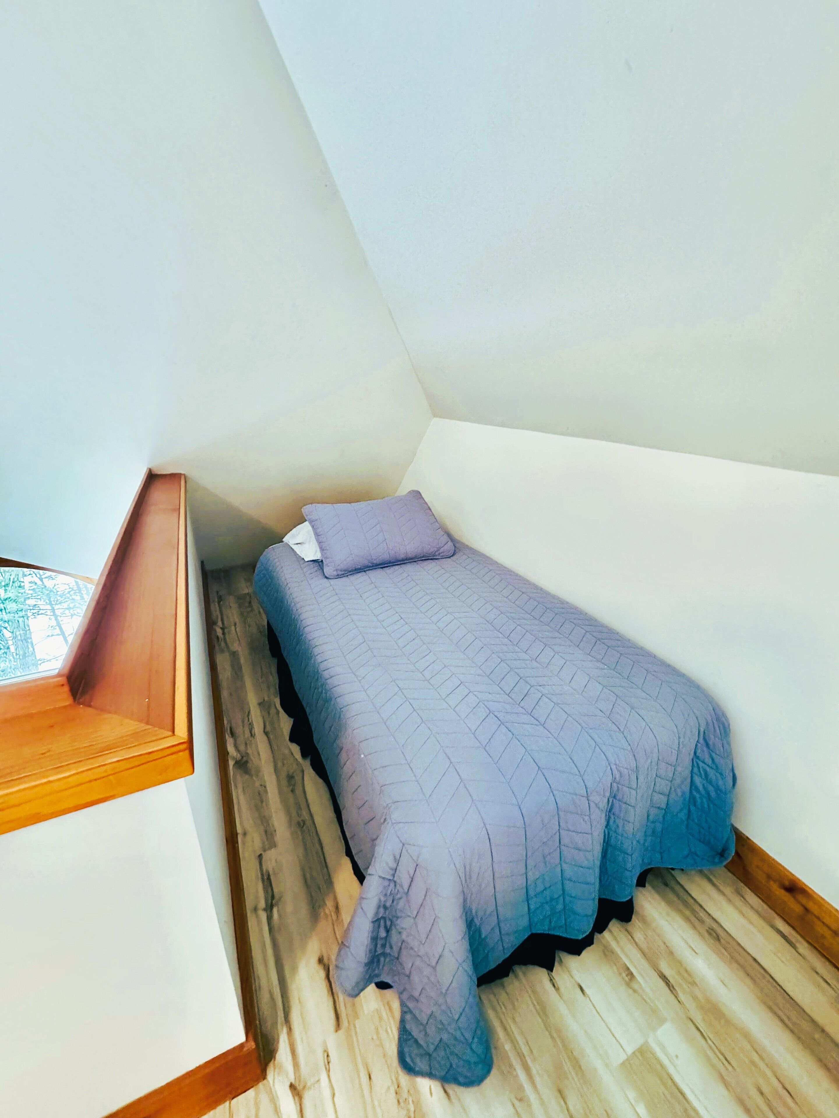 A small, single-bed room with a sloped ceiling and a wooden floor.