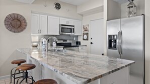 Una cocina moderna con armarios blancos, un refrigerador de acero inoxidable, un microondas y una isla grande con taburetes de bar.