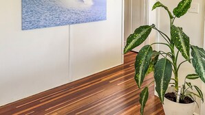 Un corridoio con pavimento in legno, un quadro appeso al muro raffigurante un'onda, una pianta in vaso e un appendiabiti.