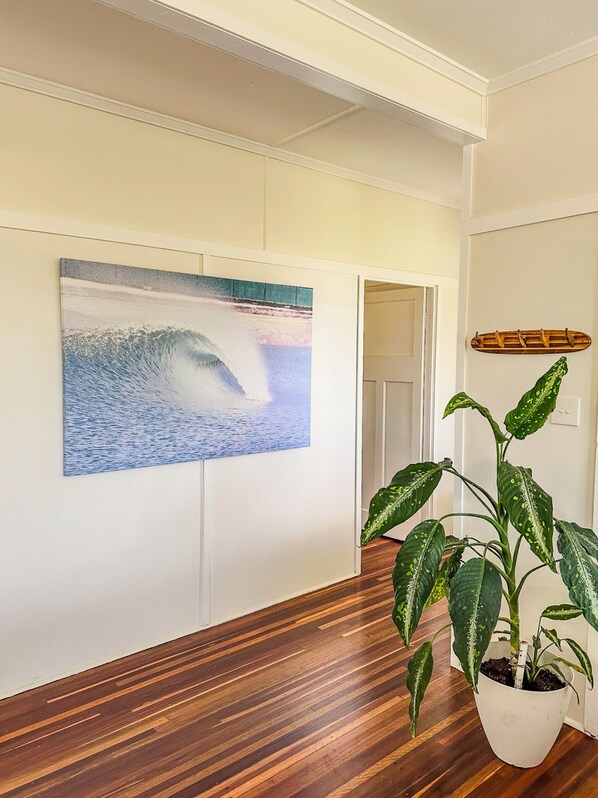 A hallway with a wooden floor, a wall-mounted painting of a wave, a potted plant, and a coat rack.