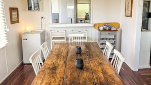 Zona pranzo con tavolo in legno, sedie bianche e cucina sullo sfondo.