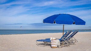 A beach with two blue lounge chairs and a blue umbrella. - Marco Island 2BR at Crystal Shores – Mid-Level Balcony, Pools & Beach Access (Marco Island)