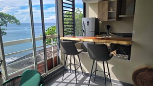 A balcony with a wooden table, two chairs, and a refrigerator.