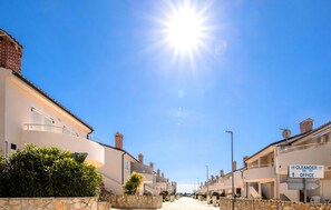 Eine Wohnstraße mit Häusern, blauem Himmel und Sonne.