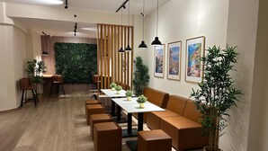 A modern dining area with wooden flooring, a long table with chairs, and a cushioned bench. There are potted plants and framed pictures on the walls. - ALMA one (Alicante)