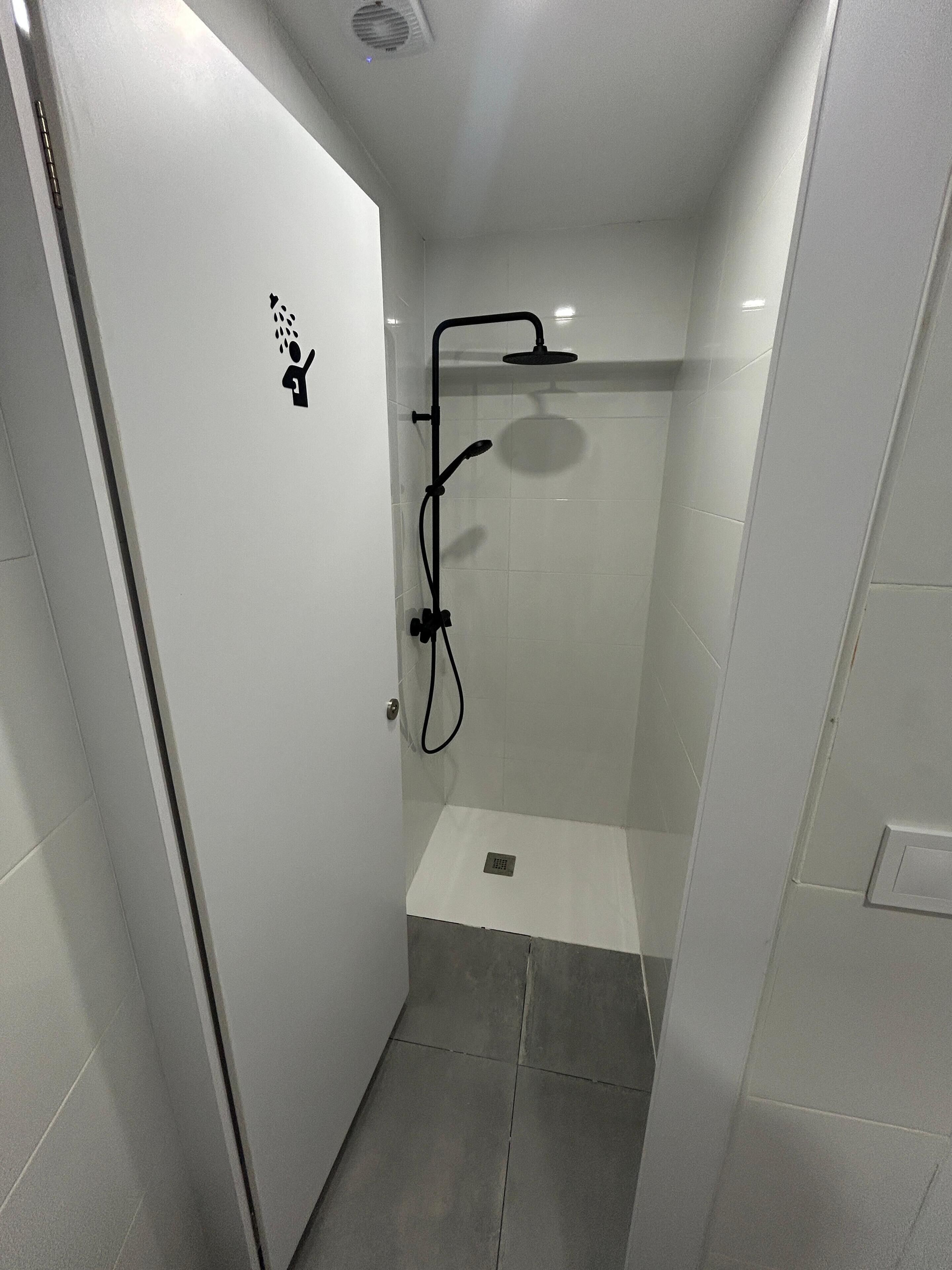 Un espacio de ducha pequeño y cerrado con puerta blanca, cabezal de ducha y un rociador de mano.