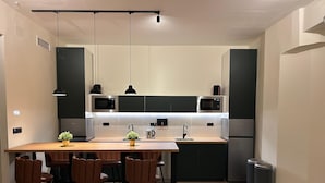A modern kitchen with a central island, black pendant lights, and stainless steel appliances. - ALMA one (Alicante)