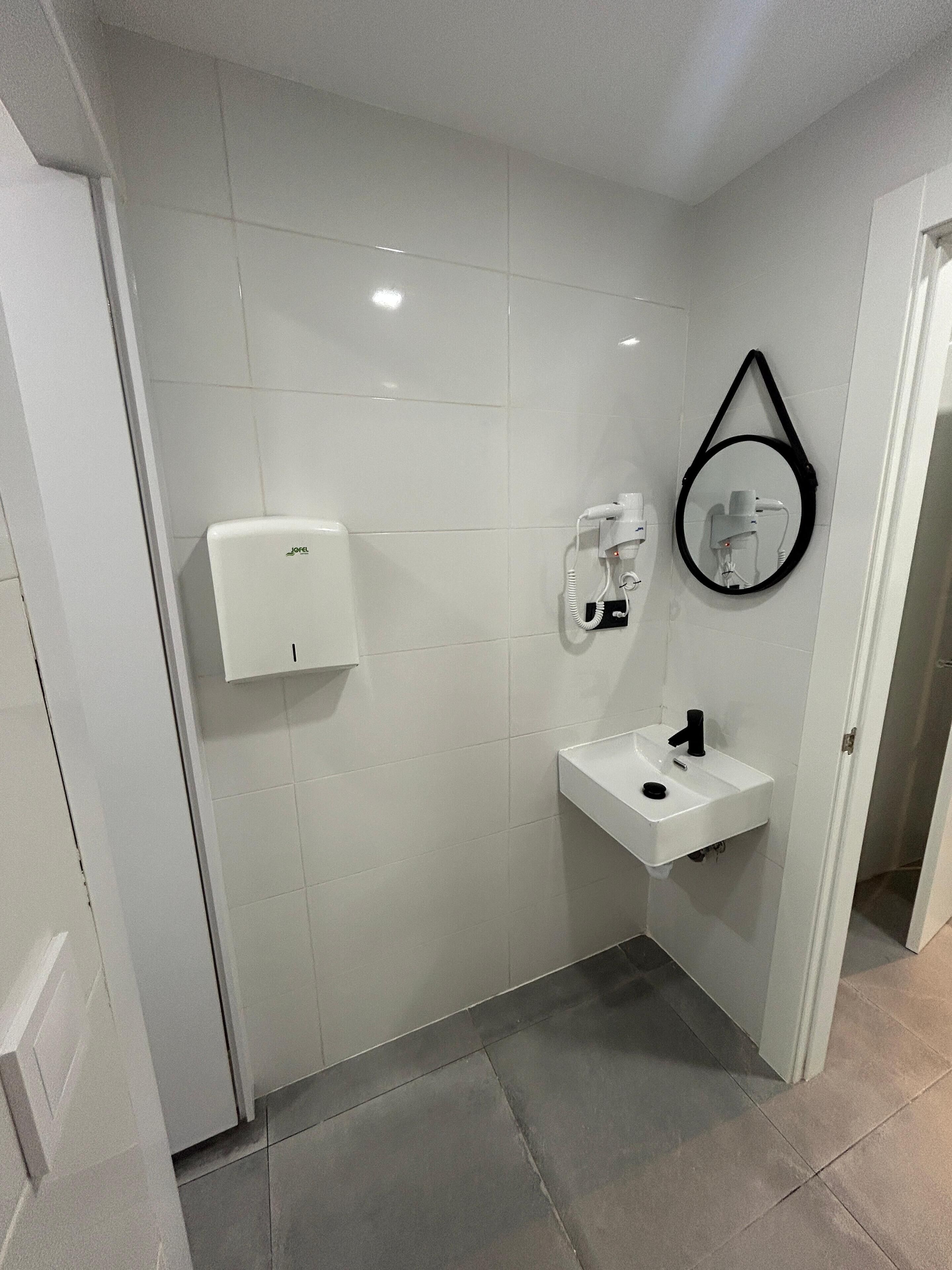 A bathroom with white tiles, a white sink, a mirror, and a hairdryer.