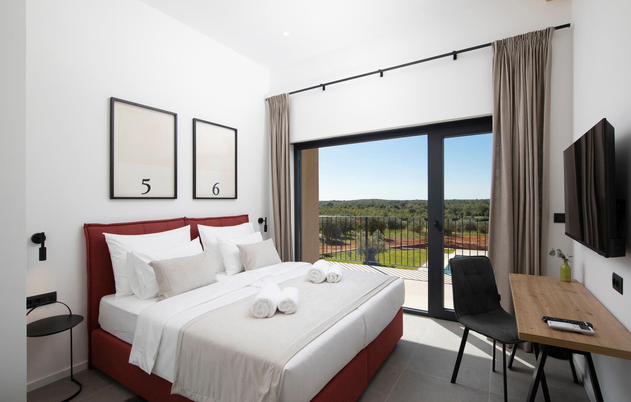 A hotel room with a bed, a desk, a chair, a TV, and a balcony with a view.