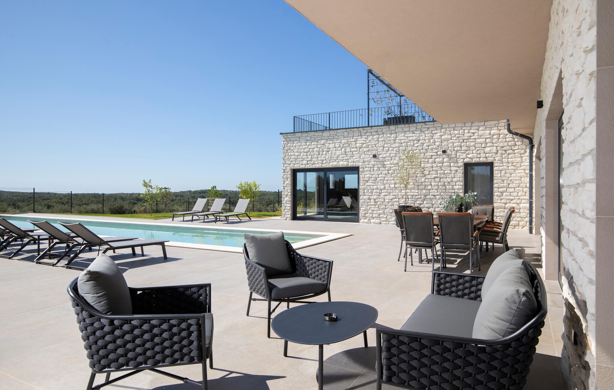Area piscina con sedie a sdraio, un tavolo e un edificio in pietra con una porta in vetro.