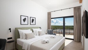 Een hotelkamer met een groot bed, een stoel, een klein tafeltje en een balkon met uitzicht.