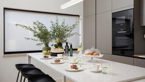 Een moderne keuken met een wit aanrecht, een Bosch oven en een eethoek met zwarte stoelen.