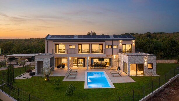 Een modern huis met twee verdiepingen, een zwembad, een gevel van natuursteen en zonnepanelen.