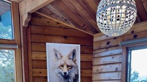 Een houten eethoek van een chalet met een tafel voor vier personen, een schilderij van een vos in een lijst aan de muur en een hanglamp.