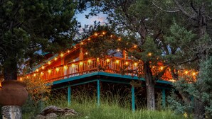 Een chalet met een houten terras en lichtjes, omgeven door bomen.
