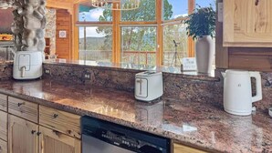 Een keuken met granieten werkbladen, een ingebouwde vaatwasser, een stenen zuil en uitzicht op het omliggende landschap door grote ramen.