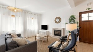 A modern living room with a sofa, armchair, TV, fireplace, and a door with an exit sign. - Second Life Baleal - 350 meters to the sea (Peniche)