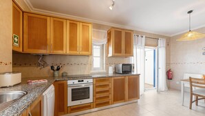 A kitchen with wooden cabinets, a built-in oven, a microwave, and a dining area with a table and chairs. - Second Life Baleal - 350 meters to the sea (Peniche)