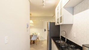 A compact kitchen with a gas stove, a refrigerator, and white cabinets. - Apt With BBQ 450m From the Beach Evu1802 (Itapema)