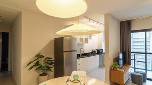 A modern kitchen with a built-in refrigerator, a dining area with a table set for two, and a large window offering a view of the cityscape. - Apt With BBQ 450m From the Beach Evu1802 (Itapema)