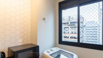 A compact kitchen with a microwave, a rice cooker, and a window with a view of buildings.