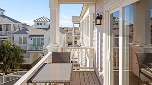 A covered outdoor balcony with a table and chairs, overlooking a residential area with multiple houses.