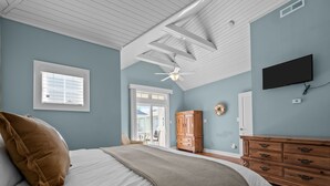 A bedroom with a bed, a ceiling fan, a TV, a wardrobe, and a view of the outside.