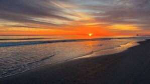 A beach at sunset with a pier in the distance.