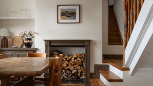 A dining area with a wooden table and chairs, a fireplace with stacked logs, and a staircase with wooden steps. - Traditional Cornish Cottage & Garden, Redruth (Redruth)