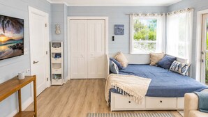 Een slaapkamer met een bed, een televisie, een boekenplank en een raam met gordijnen.