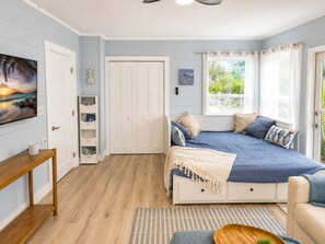 A bedroom with a bed, a TV, a bookshelf, and a window with curtains. - Resort Style Beach Retreat, Golf Cart, King Suite (Indian Rocks Beach)