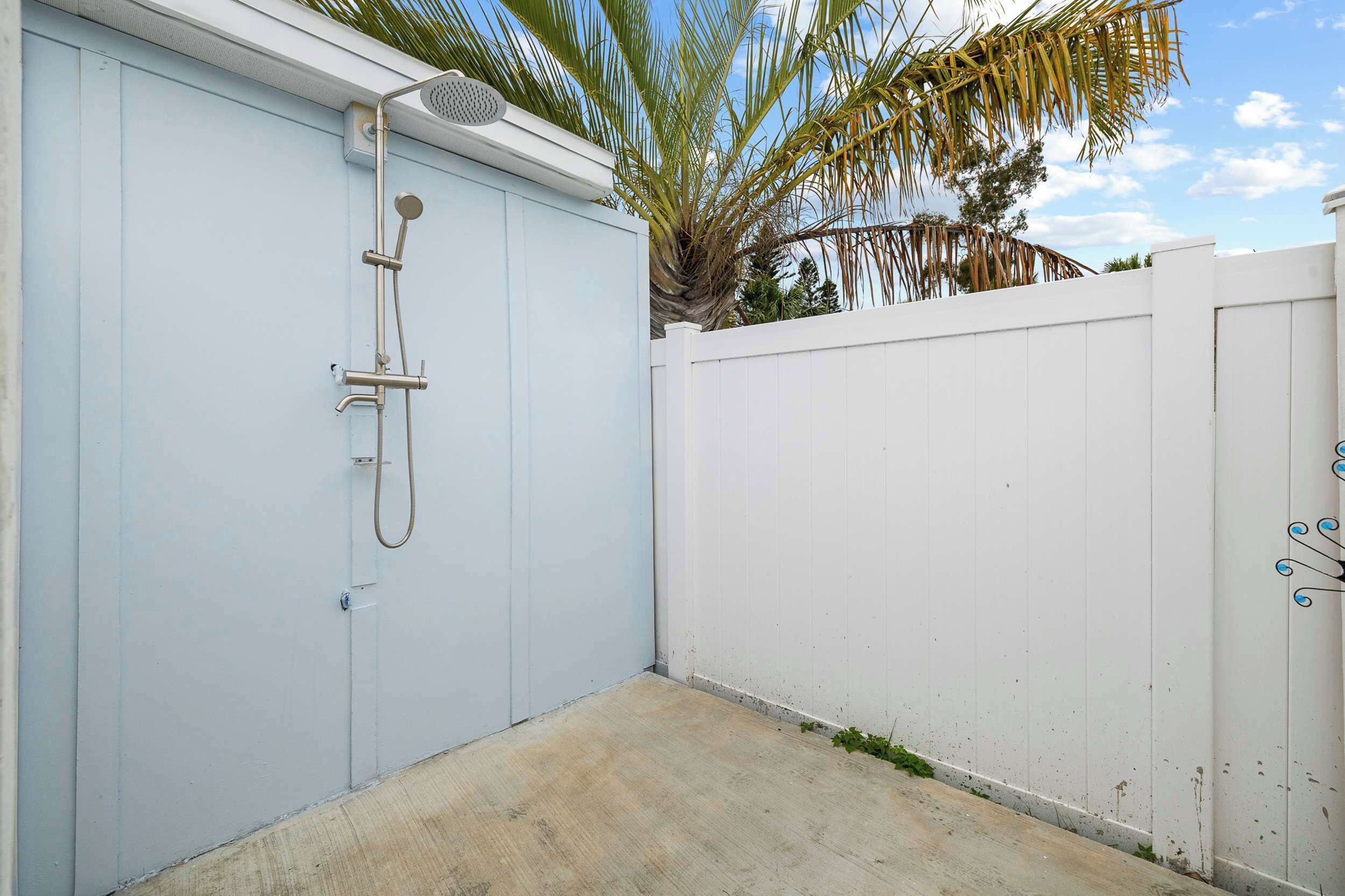 Une porte en métal blanc, avec un pommeau de douche en métal fixé au mur.