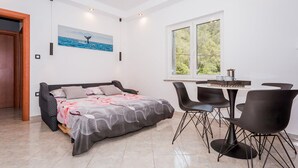 A modern bedroom with a bed, a dining table with chairs, a window with a view of trees, and a painting of a whale tail on the wall. - Lovely apartment in Brsec with WiFi (Brsec)