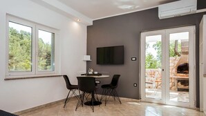 A modern living room with a dining area, a flat-screen TV mounted on the wall, and a sliding glass door leading to an outdoor patio with a stone fireplace. - Lovely apartment in Brsec with WiFi (Brsec)