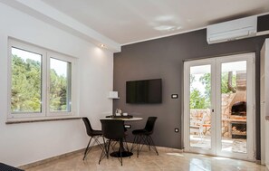 Ein modernes Wohnzimmer mit Essbereich, einem wandmontierten Flachbildfernseher und einer Glastür, die auf eine Terrasse mit Steinkamin führt.