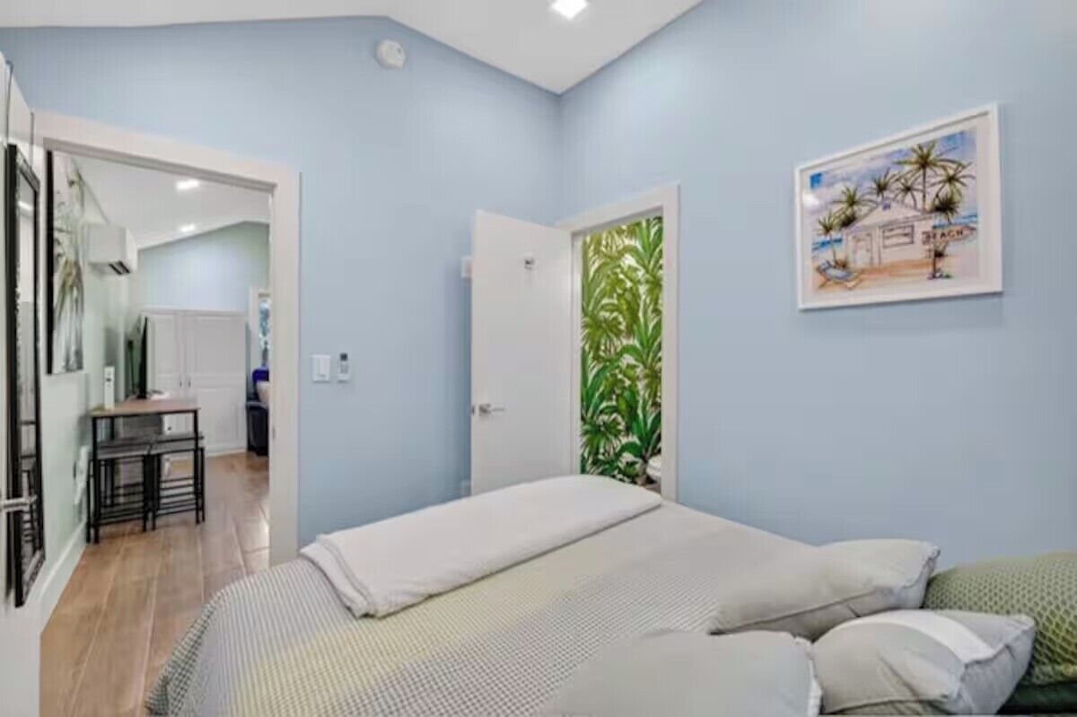 A bedroom with a bed, a desk, and a chair. There is a door with a plant on it.