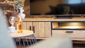 A modern living room with a flat-screen TV, wooden cabinets, a small round table with a candle, and a vase with green leaves. - ☆High quality ☆Cozy ☆Rain shower ☆Terrace ☆Garden house ☆Parking space (Neustadt/Harz)
