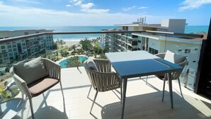 Een balkon met een tafel en stoelen, met uitzicht op een zwembad en een strand.