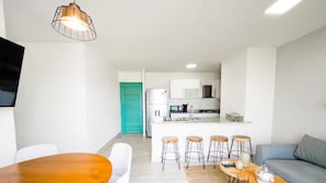 A modern living space with a dining area, kitchen, and a teal door. - Pacific Breeze -V5-5D- 2 bed, 2 bath (Punta Chame)