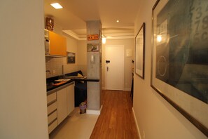 A narrow hallway with a kitchen on one side, a door at the end, and a large framed artwork on the wall. - Ape Ben Jor: a 5-minute walk from Copacabana Beach (Rio de Janeiro)