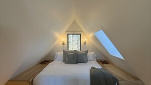 A bedroom with a sloped ceiling, a bed with pillows, a window, and wall-mounted lights. - Romantic Couples A-Frame · Hot Tub ·Outdoor Shower (Dahlonega)