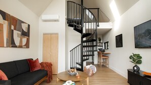 A modern living room with a black spiral staircase, a black sofa, a round wooden table, and a large abstract painting on the wall. - Romantic Couples A-Frame · Hot Tub ·Outdoor Shower (Dahlonega)