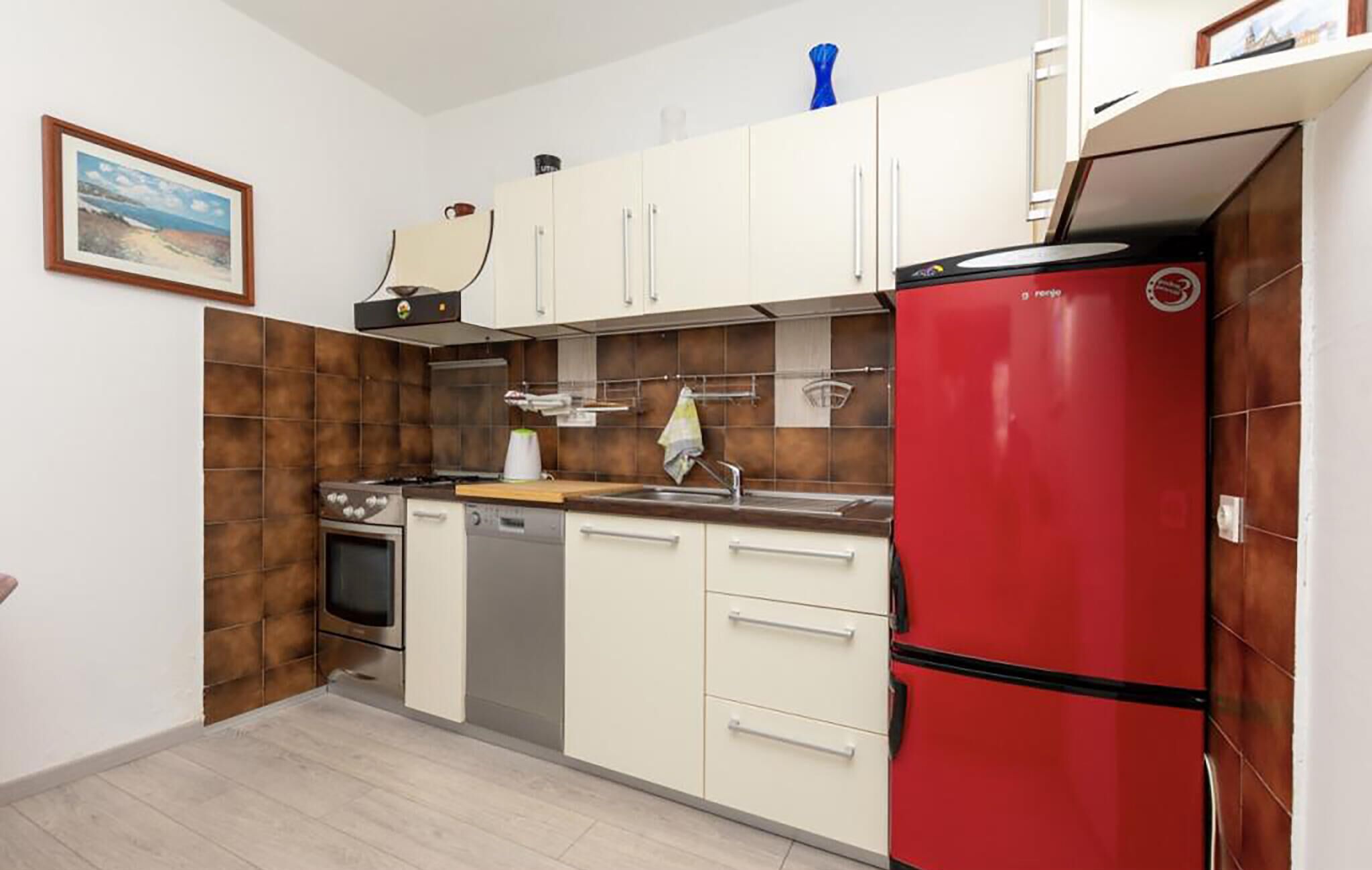 A compact kitchen with white cabinets, a red refrigerator, a stove, and a dishwasher.