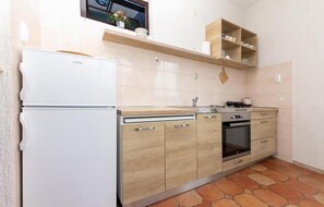Uma cozinha compacta com geladeira branca, armários de madeira, forno embutido e bancada pequena.
