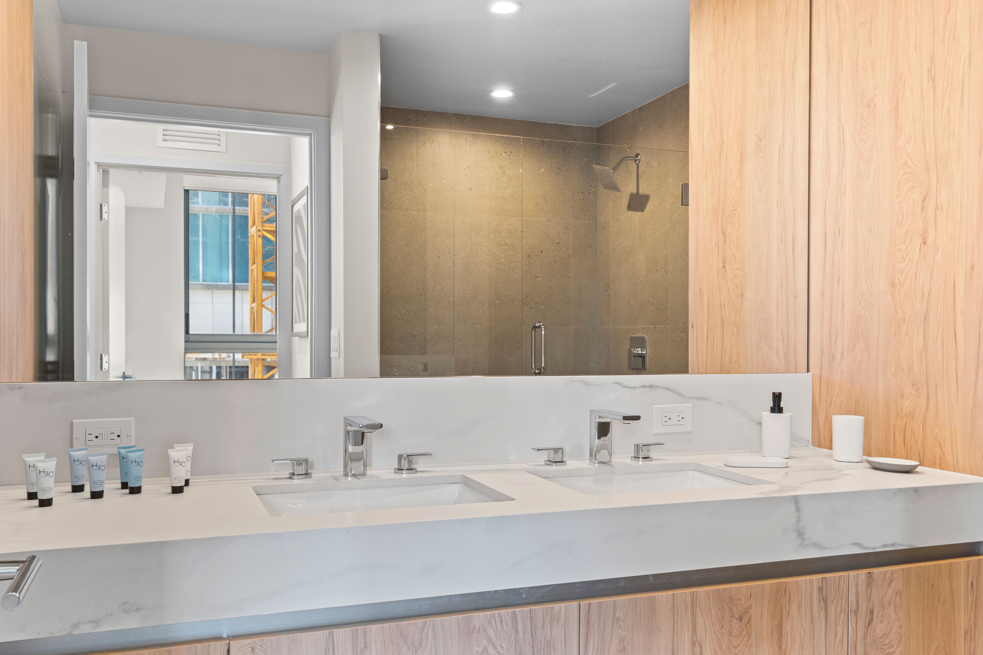 A modern bathroom with a large mirror, two sinks, and a shower area.